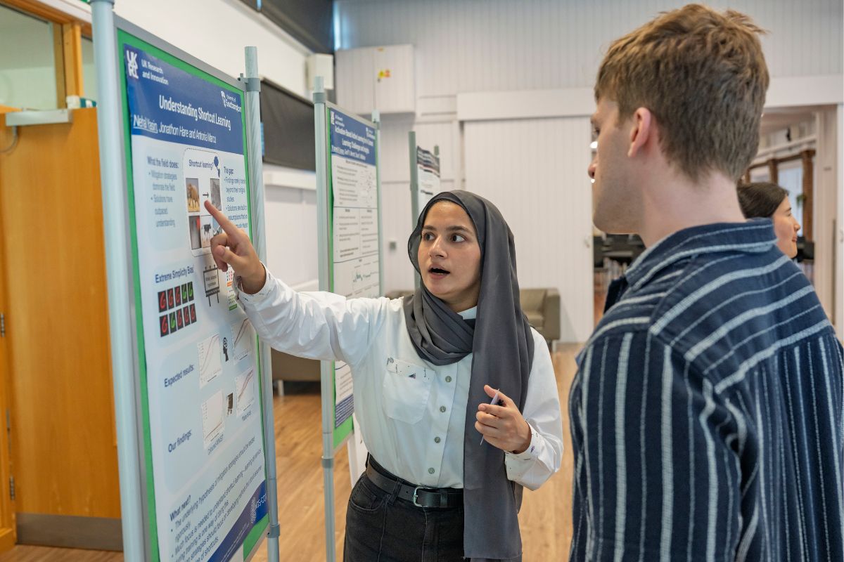 Nehal Yasin explaining her shortcut learning research poster to a visitor at the 2026 MINDS and SustAI Showcase.